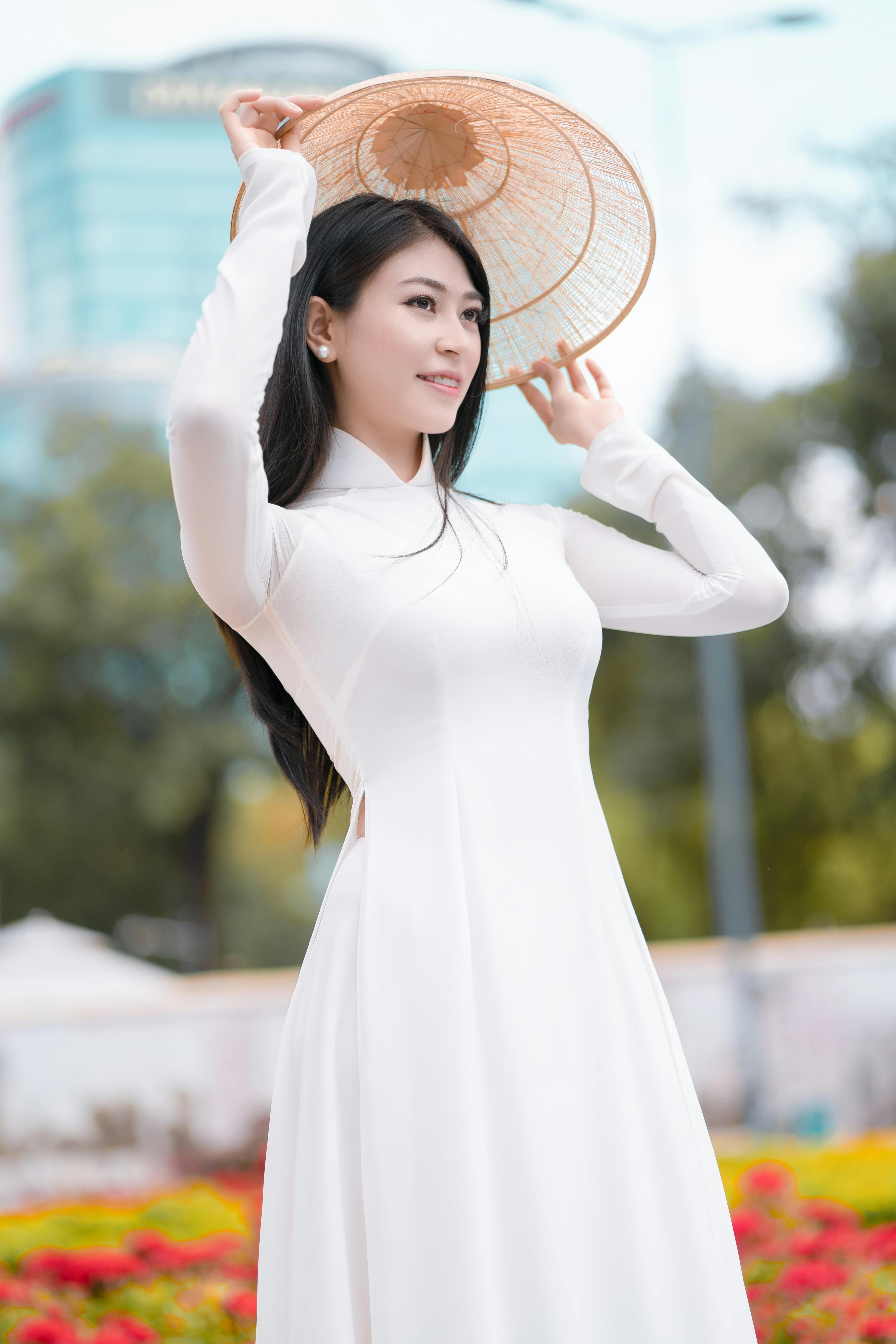 一位乐观的少数族裔女性身着优雅长裙，头戴越南传统帽子，站在公园里