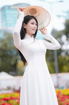 一位乐观的少数族裔女性身着优雅长裙，头戴越南传统帽子，站在公园里