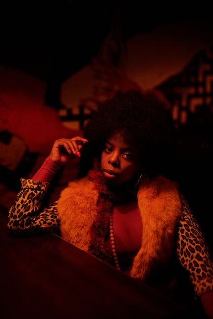 An African American woman with afro hair in leopard print clothing sitting confidently in a dimly lit bar.