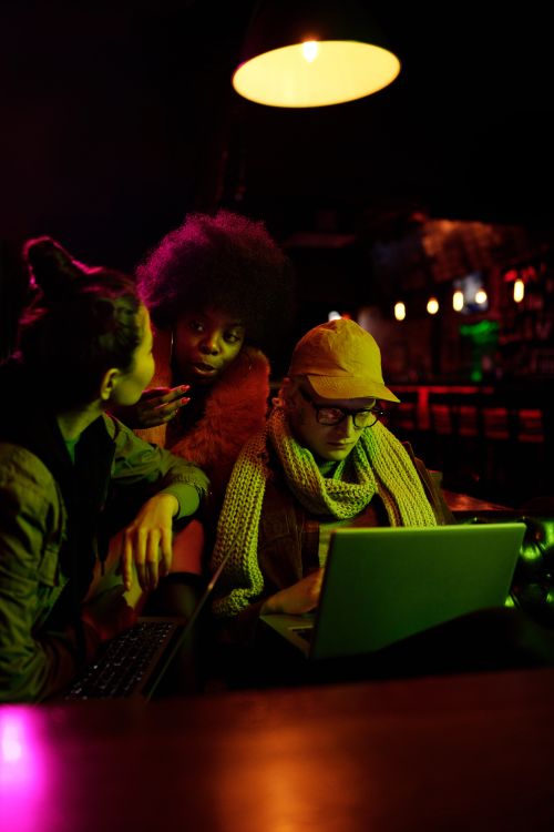 Free Three diverse friends collaborating with laptops in a dimly lit café setting. Stock Photo