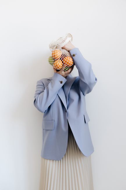 Stylish person in blue blazer holding a mesh bag with fruits, showcasing sustainable living.