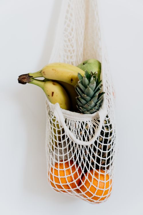 Free Sustainably sourced bananas, oranges, and pineapple in a reusable mesh bag against a white background. Stock Photo