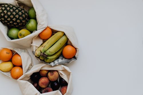 Free A top-down view of various fresh fruits like apples, bananas, and oranges in cotton bags on a white background. Stock Photo