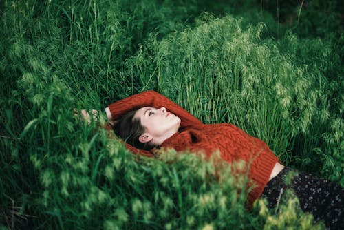 Free Serious young beautiful female in sweater and skirt looking up while chilling on lawn with hand behind head Stock Photo