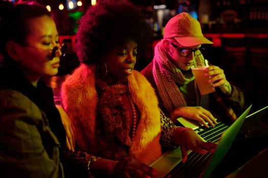 A diverse group of friends using laptops in a cozy, illuminated indoor setting.