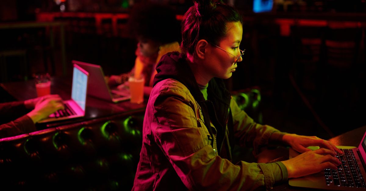 person wearing blue light blocking glasses while working on a laptop in a dimly lit room
