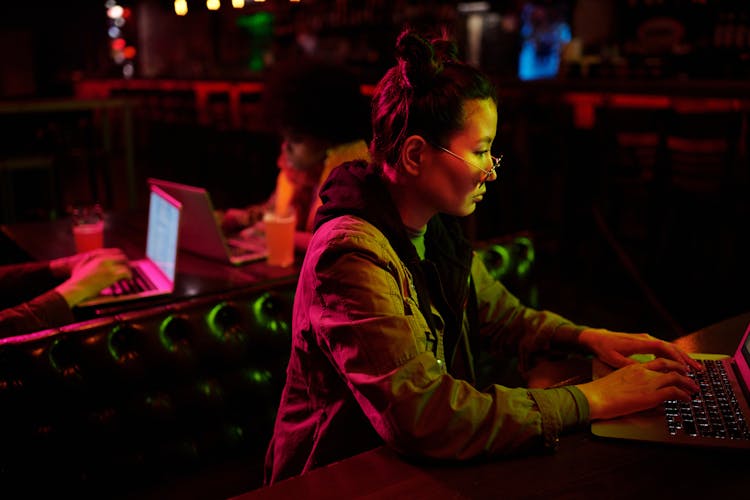 A Woman In A Dark Room Typing On Her Laptop