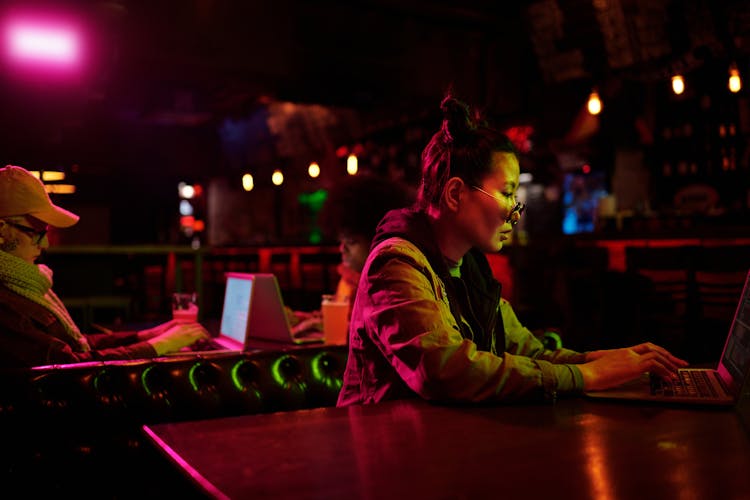 A Woman In A Dark Room Typing On Her Laptop