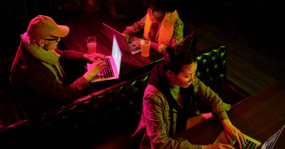 A young person coding on a laptop in a coffee shop, looking confident and creative