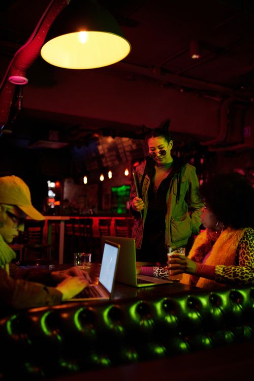 Free Friends socializing in an urban pub, enjoying drinks and online entertainment. Stock Photo