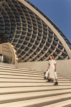 A fashionable woman in a white dress and black boots descends a modern architectural staircase.