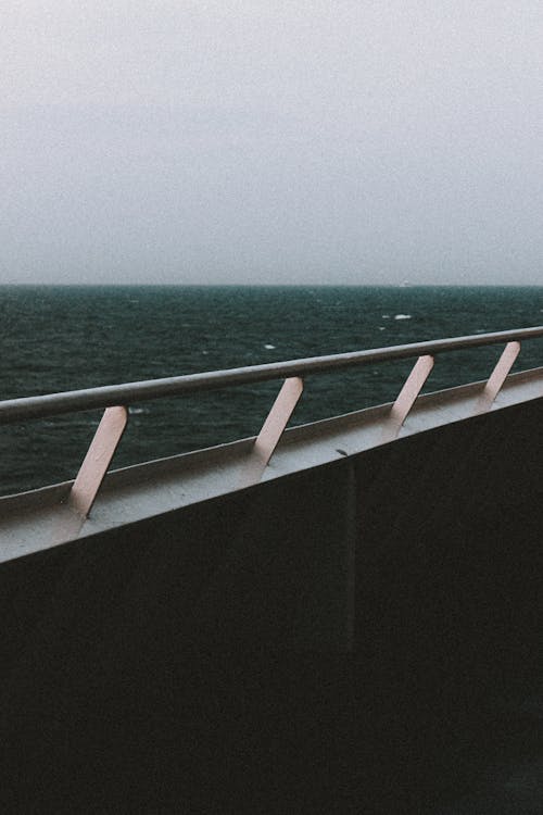 Grey sky above dark calm endless ocean and long white railing of cruise ship in daylight