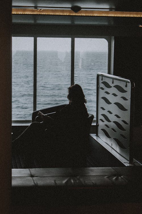 Side view of anonymous voyager resting in chair next to window in dark room in cruise ship