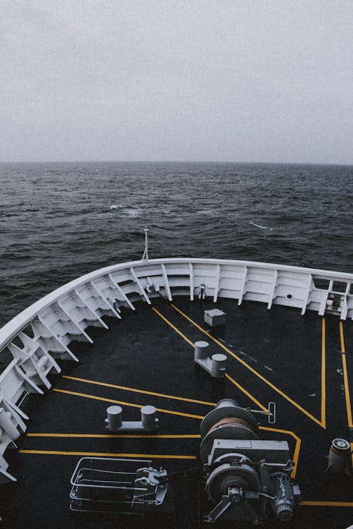 Grey sky above calm water surface of dark endless ocean and front of ship