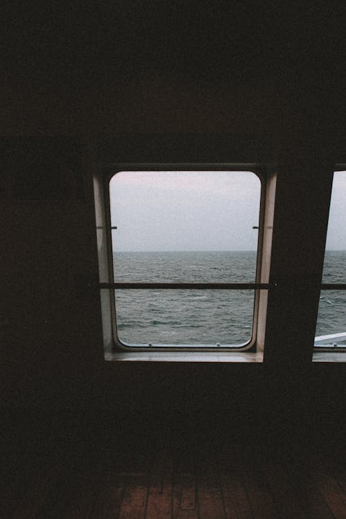 Grey sky above dark silent endless ocean from window of dark gloomy room with wooden floor on cruise ship