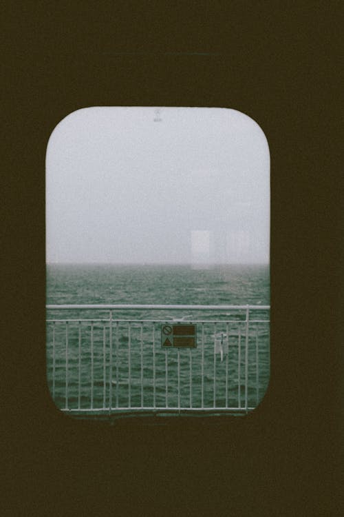 Dark endless ocean and fence on simple balcony on cruise ship from window from dark gloomy cabin
