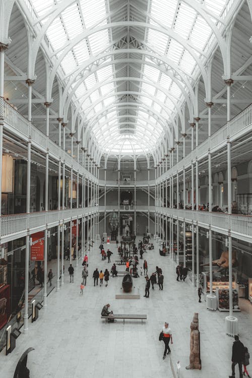 Interior of bright spacious hall with balconies and windows on high ceiling and benches and statue on floor