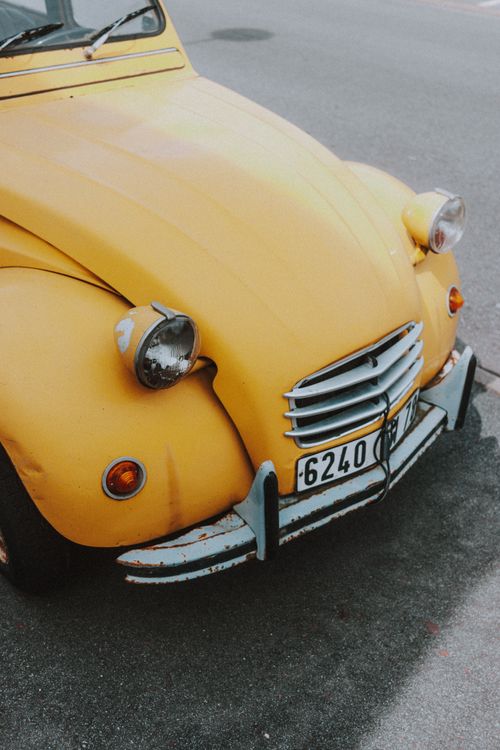 Free Small round transparent and read headlights and metallic license plate above numbers of vibrant old shabby car on paved road in daylight Stock Photo