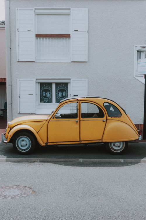 Free Small yellow old car parked on pavement next to white wall of big building Stock Photo