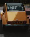 Numbers on license plate and square red backlights of old shabby rust yellow retro car on paved road in sunlight