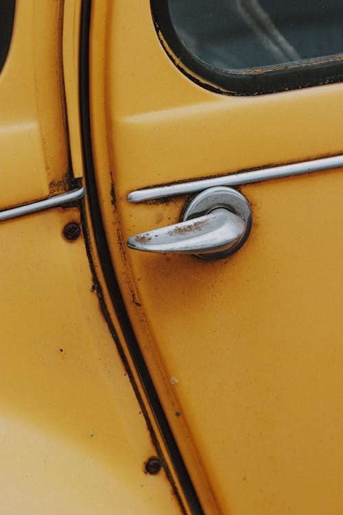 Small metallic rusty handle on side door of old yellow shabby retro car in daylight