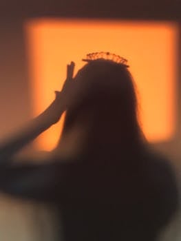 A silhouette of a person wearing a crown with a warm orange background.