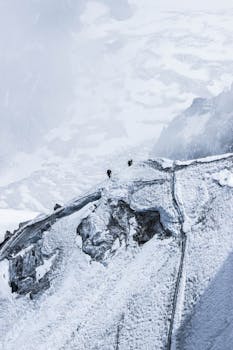 Two mountaineers ascend a breathtaking snowy ridge amidst a majestic mountain landscape.