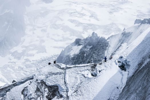 From above distant brave alpinists in winter clothes climbing on rough stiff mountain slope covered with ice and snow on high altitude