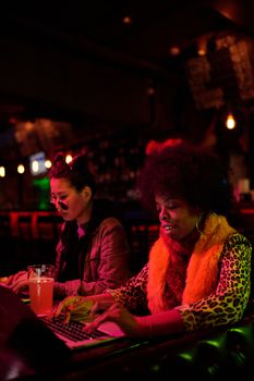 Two women typing on laptops in a warmly lit bar, creating a cozy work atmosphere.