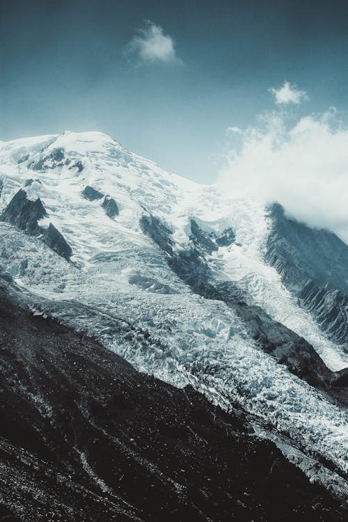 Severe rocky mountain slope covered with thick layer of snow against blue sky