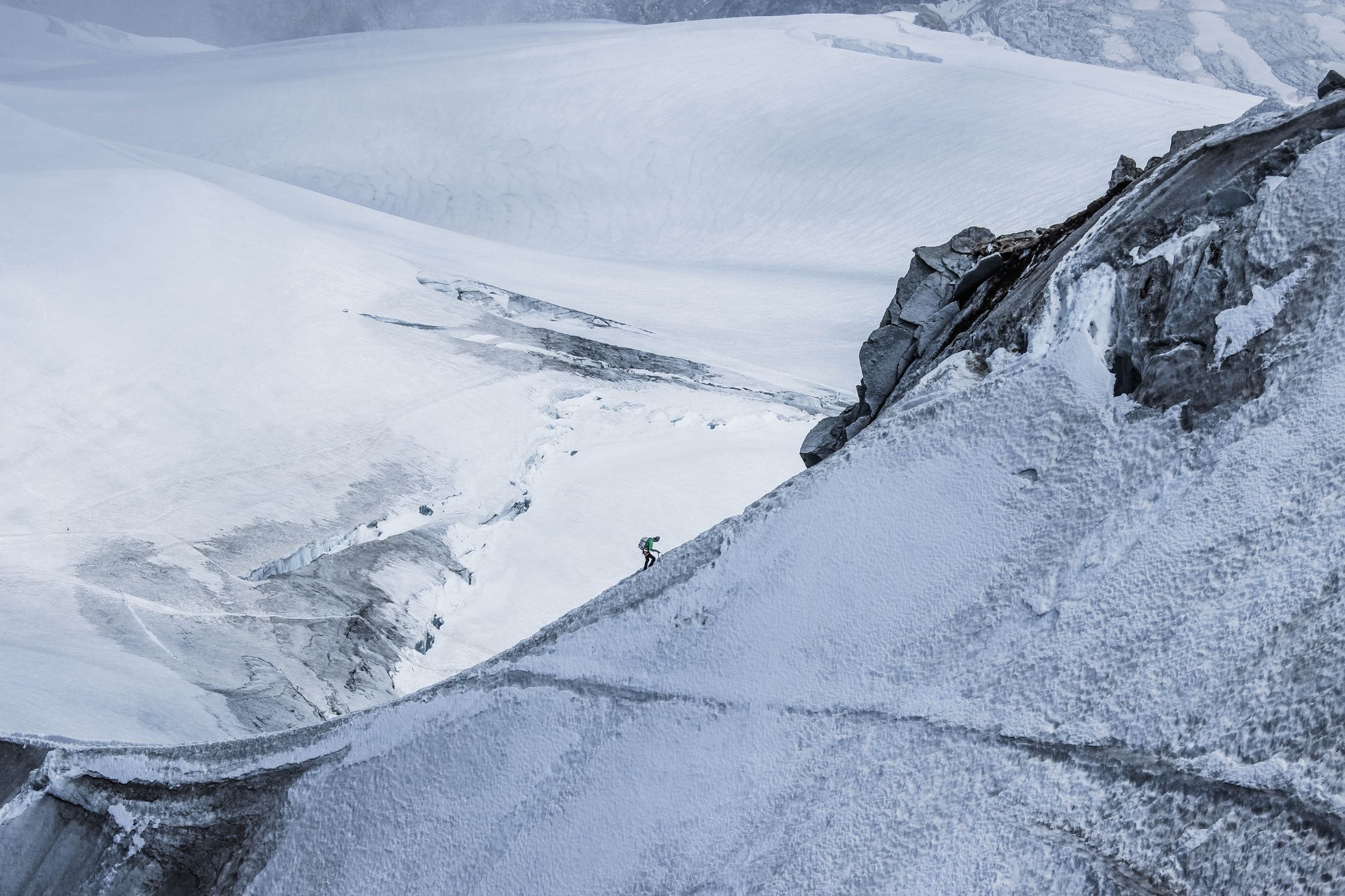 Distant alpinist on a snowy mountain slope with a frozen mountainous valley below