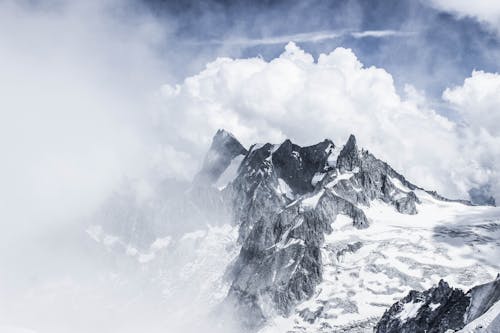 Free Majestic rough mountains with rocky peaks under thick layer of snow against cloudy misty sky Stock Photo
