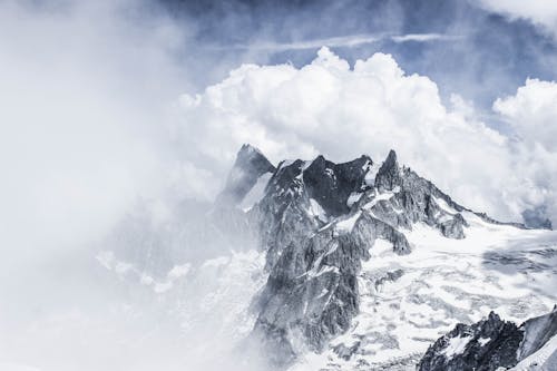 Majestic rough mountains with rocky peaks under thick layer of snow against cloudy misty sky