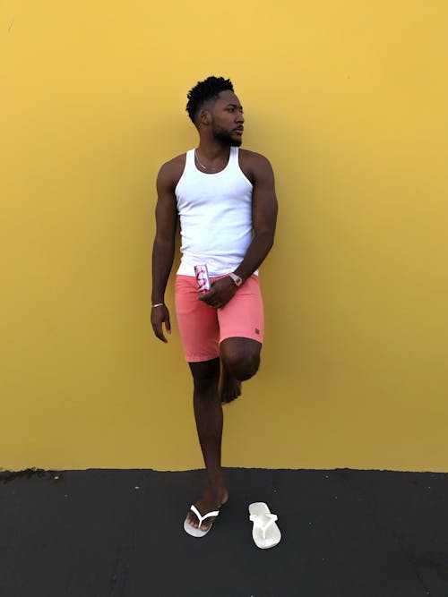 Photo of a Man in a White Tank Top Leaning on a Yellow Wall