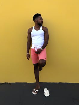 Casual portrait of a stylish man in summer attire against a vibrant yellow wall.
