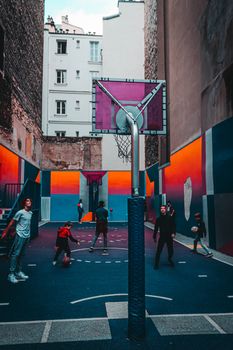 Teenagers in activewear playing basketball on colorful modern sports ground located between tall urban buildings