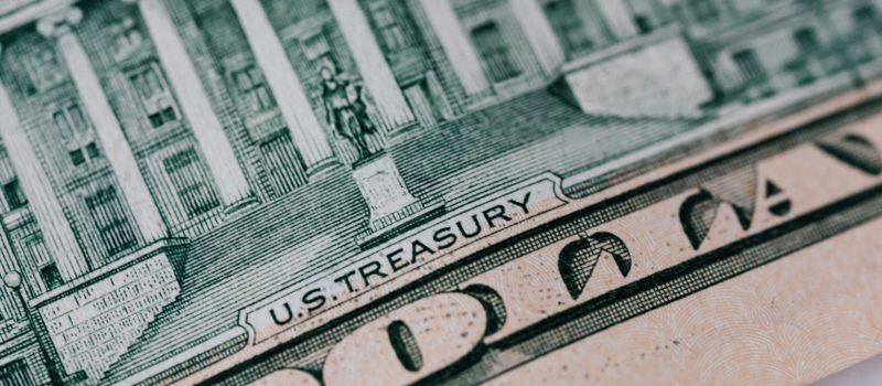 米財務省庁舎の上に置かれた10ドル紙幣のイメージ。国債買い戻し策のニュースに合わせ、米国の金融政策の舞台を象徴的に示す。