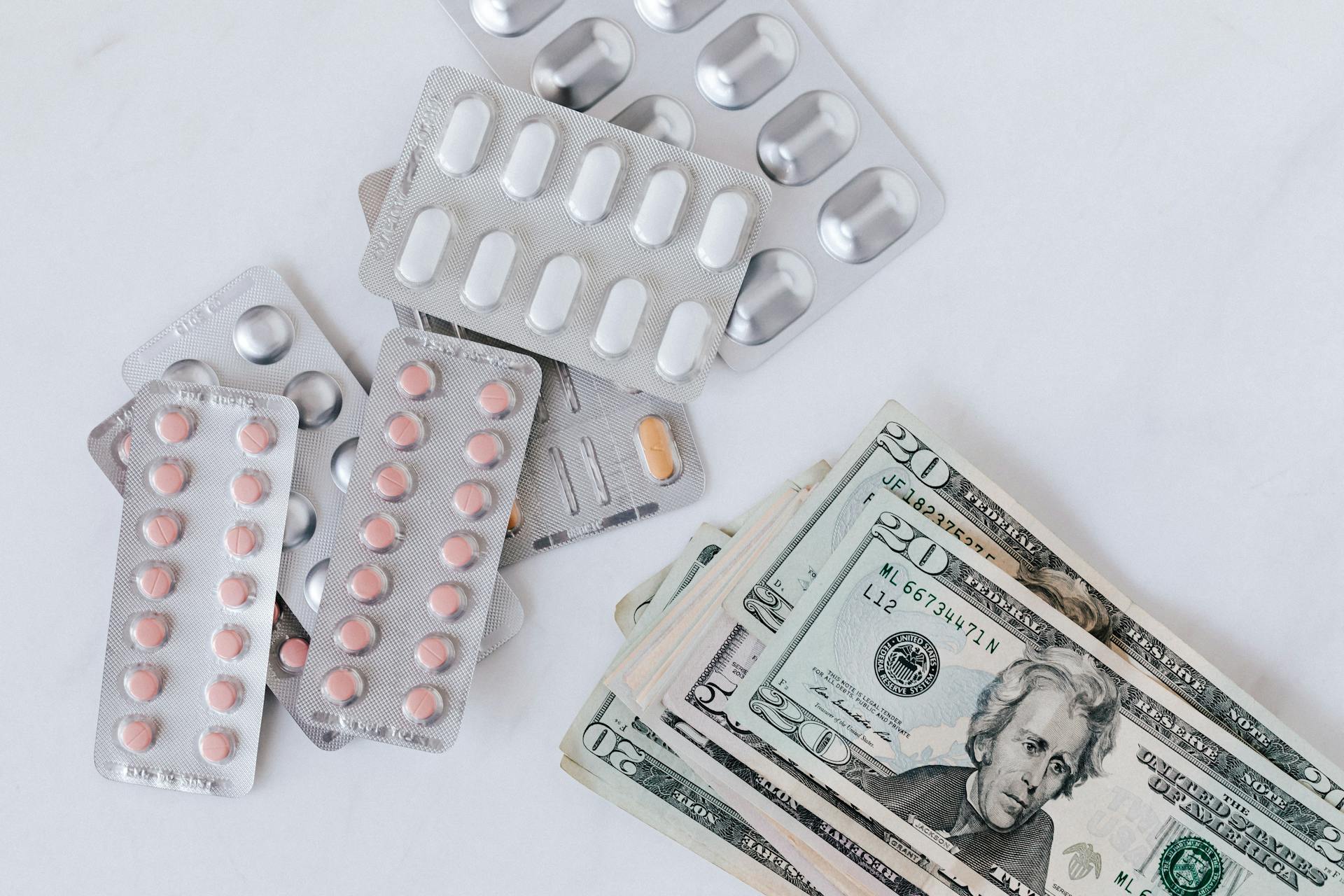 Top view of different blisters of medications and pills composed with heap of paper money