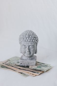 一尊石佛半身像被放置在一堆美元纸币上，象征着和谐与金融