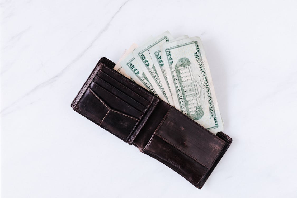 Free From above of black leather wallet with pockets filled with heap of dollar banknotes on white table Stock Photo