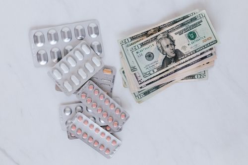 Free From above of silver blister full of drug near big pile of dollar to spend on medication Stock Photo