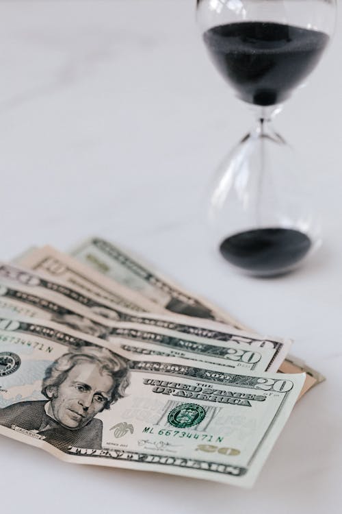 Free From above of transparent hourglass with black sand and heap of American dollars with image of president Stock Photo
