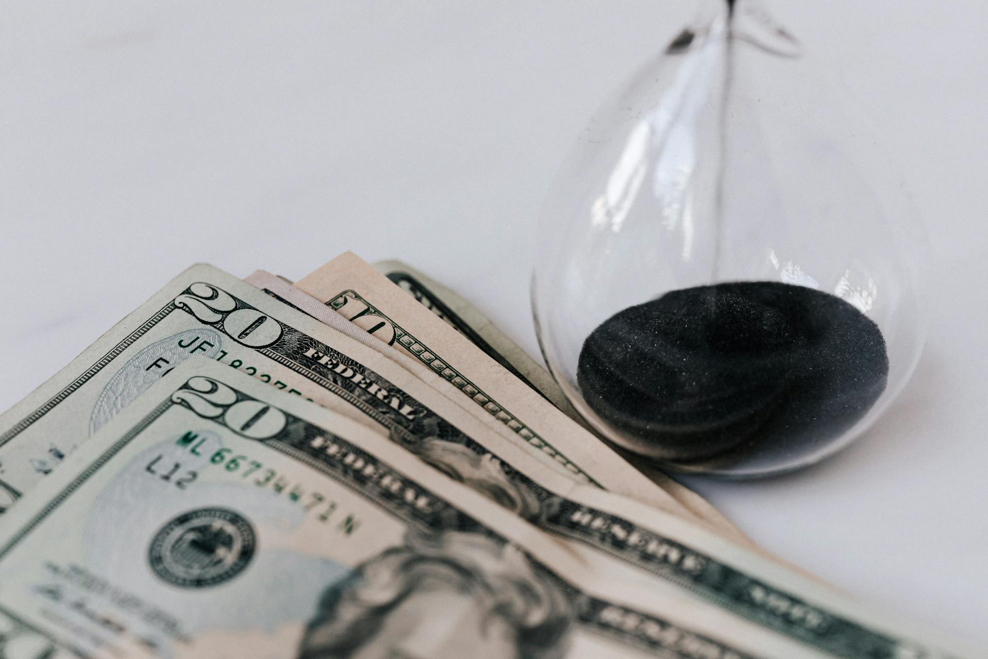 From above transparent hourglass with flares on fragile surface near pile of banknotes with numbers and official seal