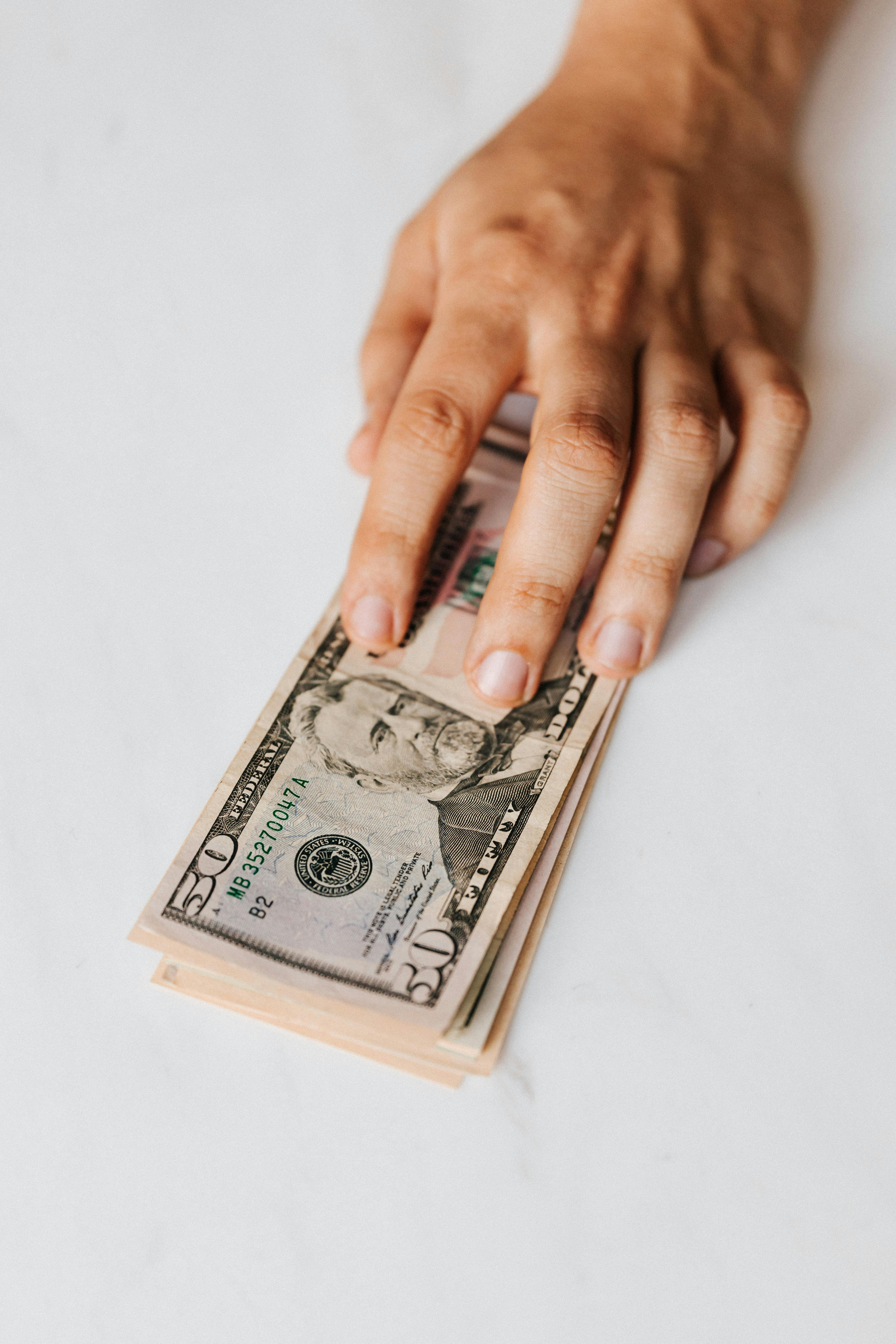 crop faceless person putting pile of paper money on table