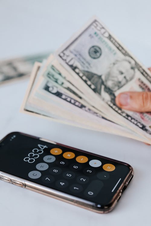 Free From above of crop anonymous person holding heap of American dollar near cellphone with calculator application representing numbers Stock Photo