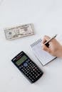 特写镜头对准笔记本上的手写内容，桌上放着计算器和美元钞票，重点突出预算
