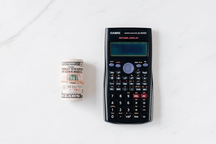 Modern Calculator And Roll Of Paper Money On Marble Table