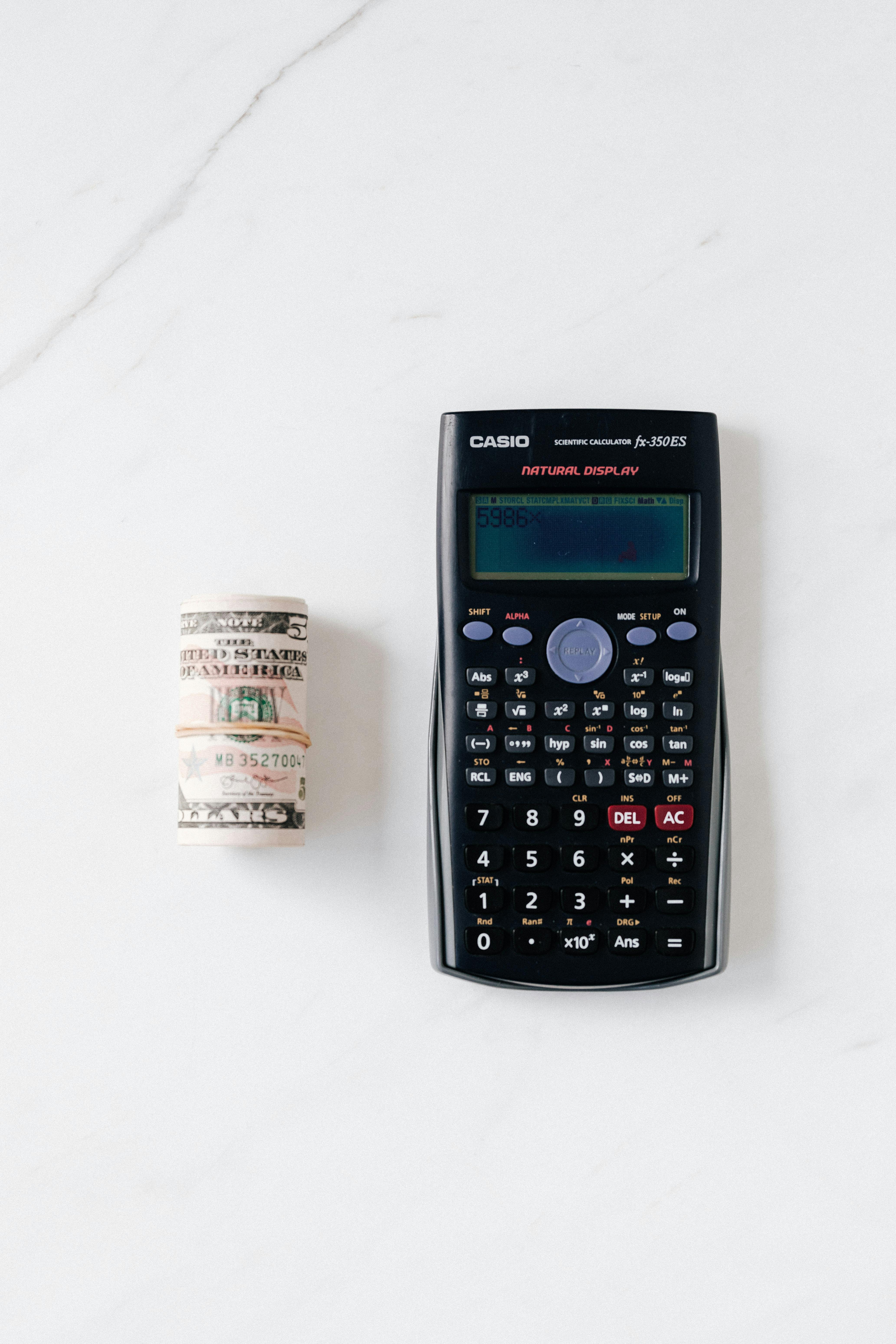 composition of electronic calculator and roll of greenbacks on table