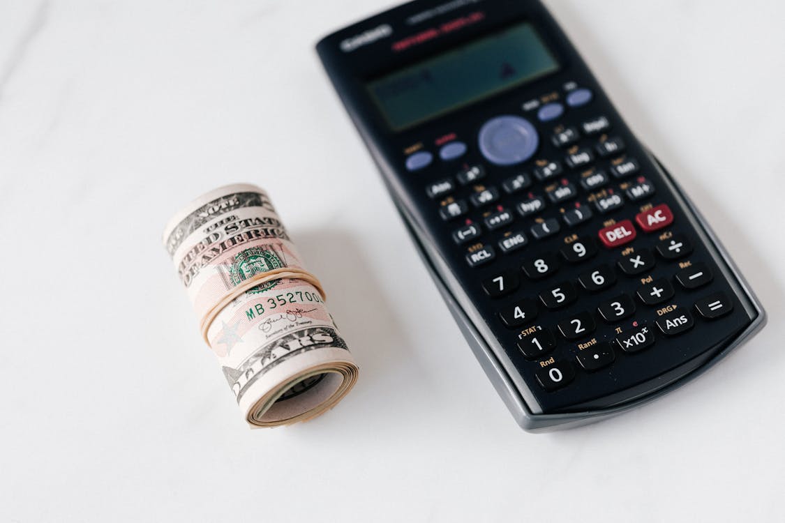 Free From above of modern electronic calculator with small display and buttons of different colors near roll of dollar bills on marble surface Stock Photo