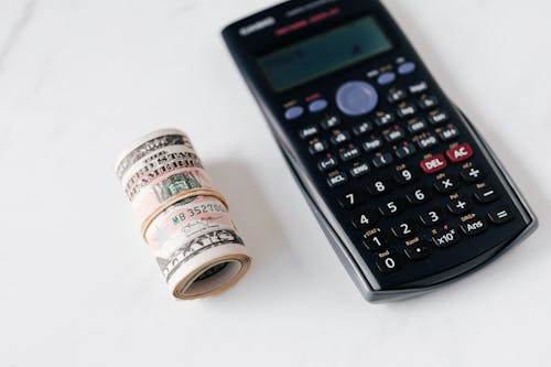 From above of modern electronic calculator with small display and buttons of different colors near roll of dollar bills on marble surface